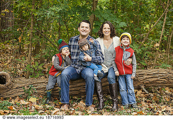 a smiling family sit together on a log in the woods