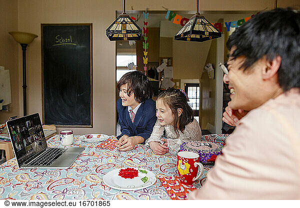 A smiling family sits at table on a zoom meeting birthday party
