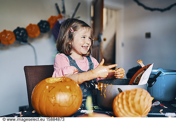A smiling girl taking the pumpkin seeds and flesh from her fingers.