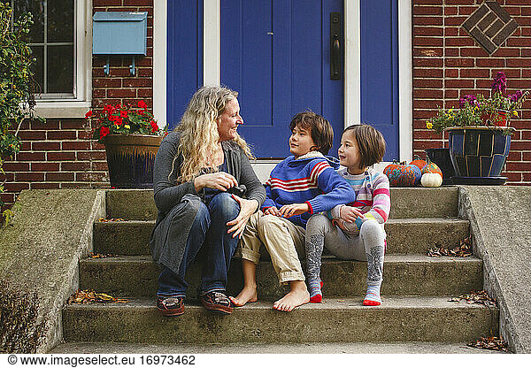 A smiling Mom sits with her two children on front stoop of home