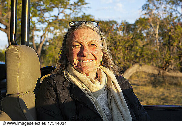 A smiling senior woman seated in a jeep at sunset  smiling.