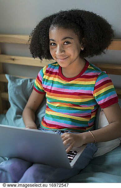 A smiling ten year-old bi-racial girl works on her apple laptop
