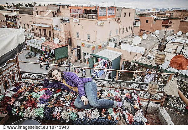 A smiling woman relaxes on a rooftop overlooking Marrakesh  Morocco