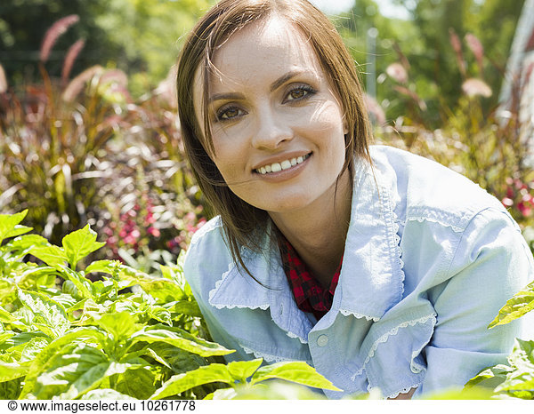 A smiling young woman surrounded by plants in a garden or garden centre.