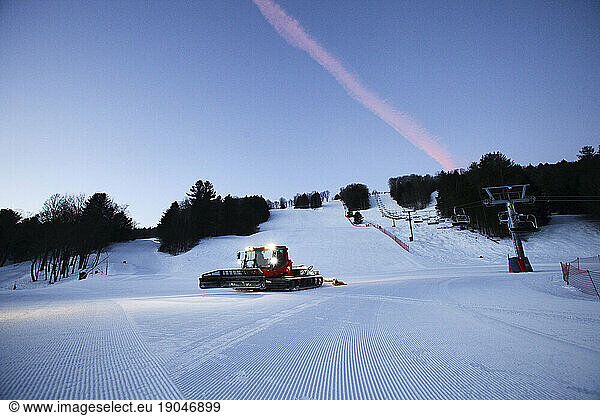 A snow cat grooms fresh snow as the sun rises at a Vermont ski hill