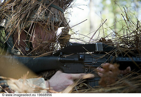 A solider uses brush and twig as concealment during ambush training.