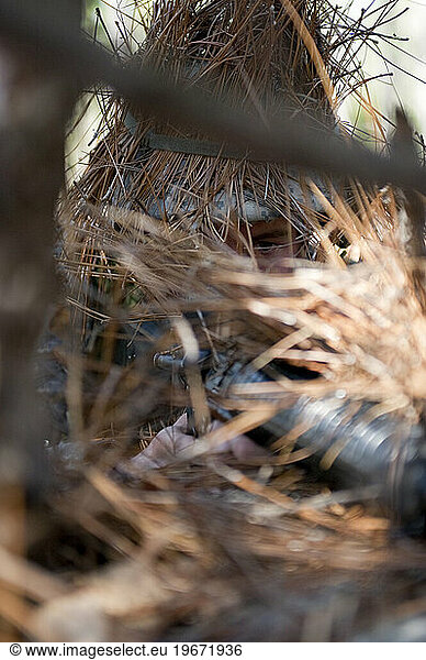 A solider uses brush and twig as concealment during ambush training.