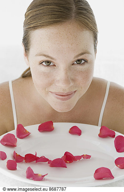 A spa treatment centre. A young woman with a white dish of pink rose petals.