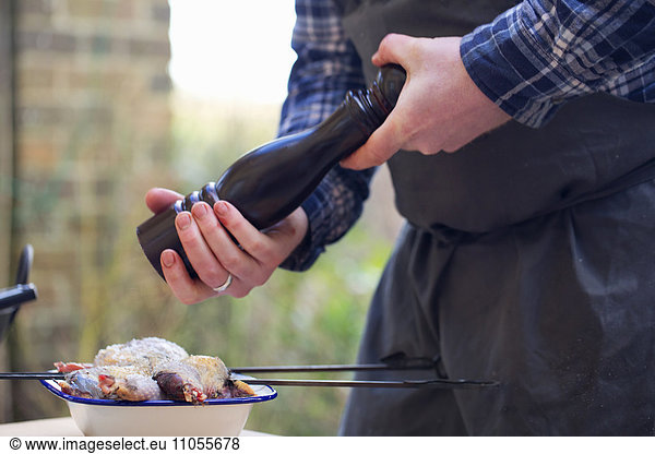 A spatchcocked game bird being seasoned for cooking,  a man's hand grinding pepper in a mill.