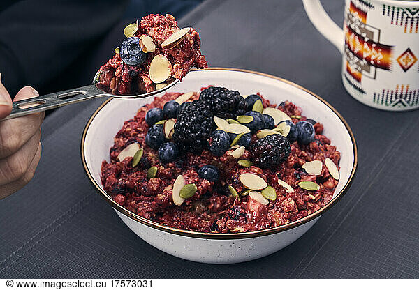A spoon scoops breakfast cereal with fresh blackberries and almonds.