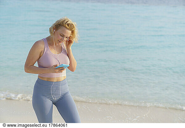 A sporty woman looks at her smartphone on the beach.