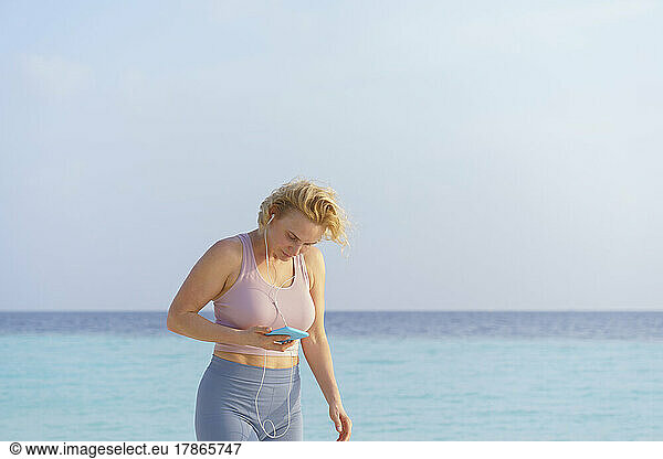 A sporty woman on the beach listens to music on her smartphone.