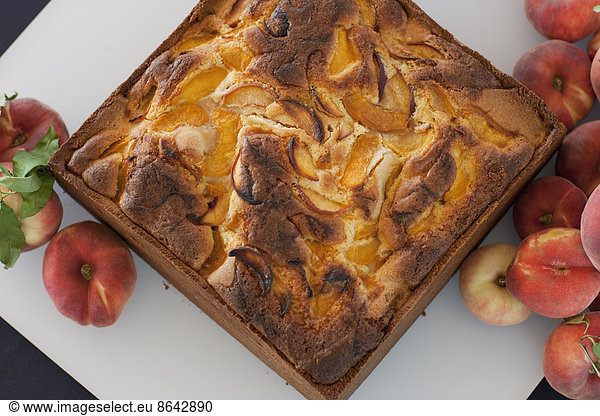A square baked peach cake on a board with fresh peaches. Fruits. Organic fresh food on a farm stand.
