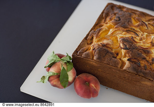 A square baked peach cake on a board with fresh peaches. Fruits. Organic fresh food on a farm stand with a herb garnish.