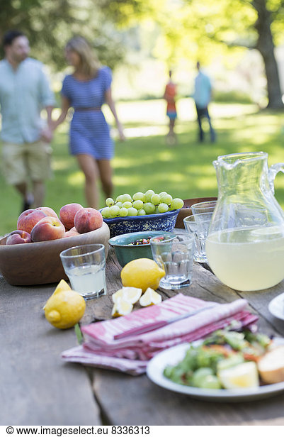 A summer buffet of fruits and vegetables  laid out on a table. People in the background.