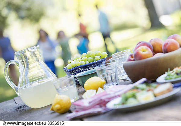 A summer buffet of fruits and vegetables  laid out on a table. People in the background.