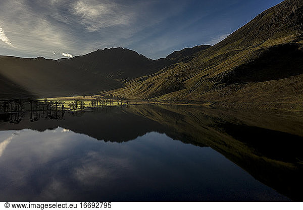 A sunrise over buttermere lights up trees on the shore line