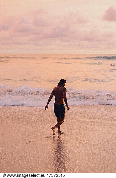 a surfer walking to the ocean during the sunset