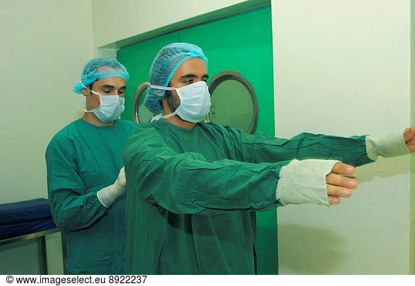 A surgeon preparing for surgery  his assistant helps him with his surgical drapes.