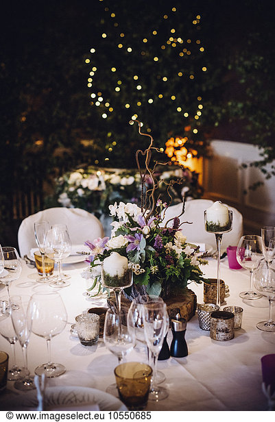 A table laid for a special occasion  with a floral centrepiece and candles  at night.