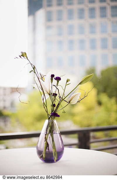 A table on a terrace in the city. A vase of flowers. Small purple flowers  and white lily and orchid blooms.
