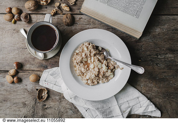 A table with a cup of coffee  bowl of muesli  nuts and an open book.