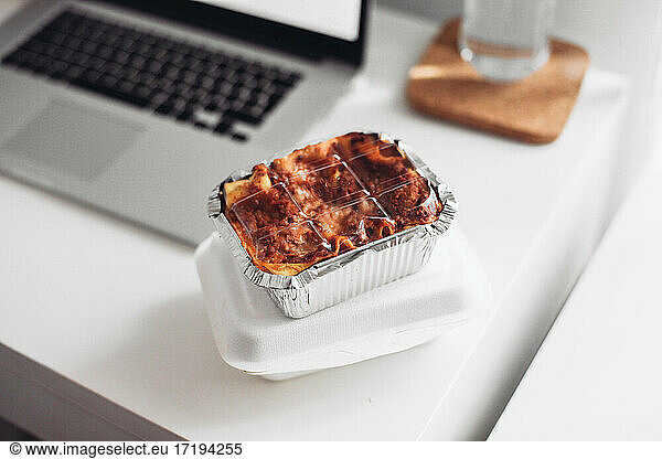 A takeaway box with lasagna  a laptop. Concept of eating at home