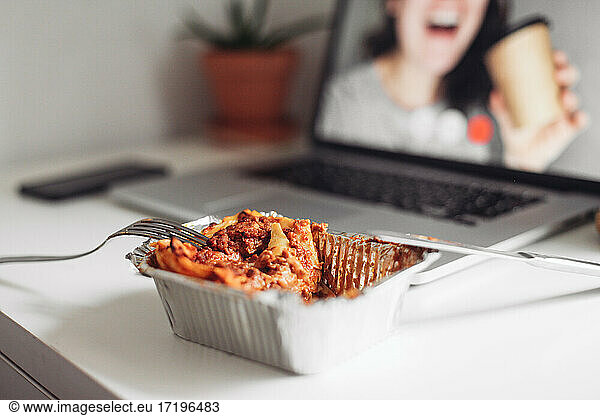 A takeaway box with lasagna  laptop with a video call with a girl