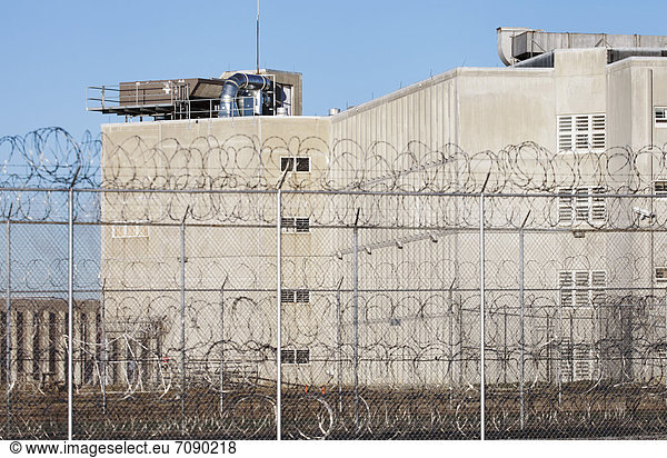 A tall building in a prison complex  with a barbed wire fence at Correctional Facility.