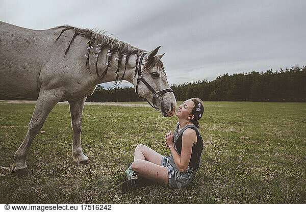 A teen girl sitting with grey horse with braids and flowers