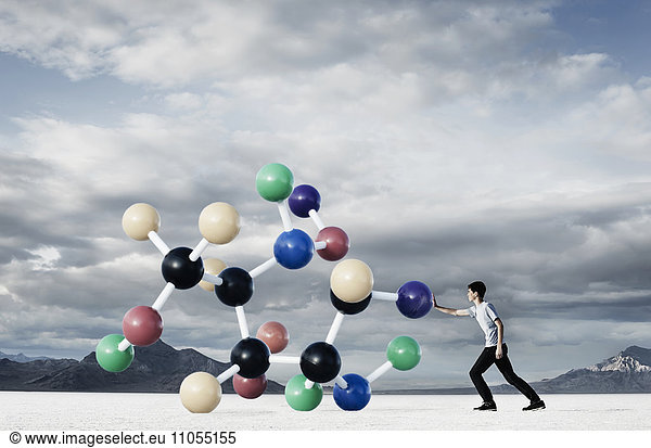 A teenage boy putting his hand out to push a large molecular structural model away from him.