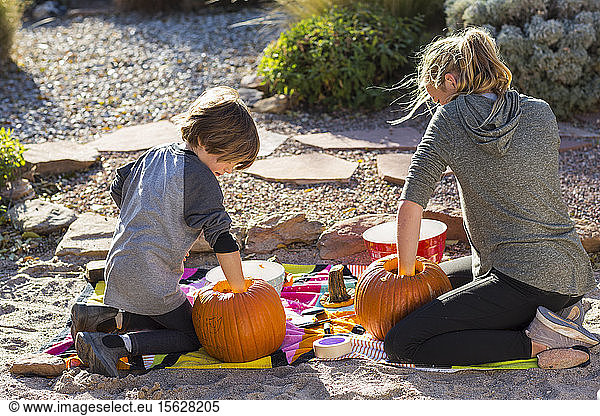 A teenage girl and her brother carving pumpkins at Halloween.