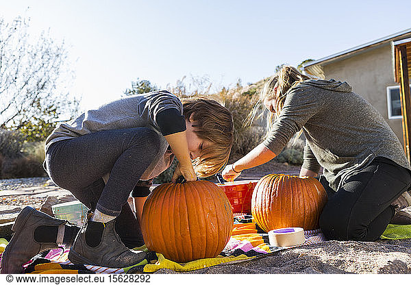A teenage girl and her brother carving pumpkins at Halloween.
