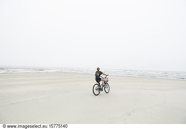 A teenage girl biking on a sandy beach by the ocean