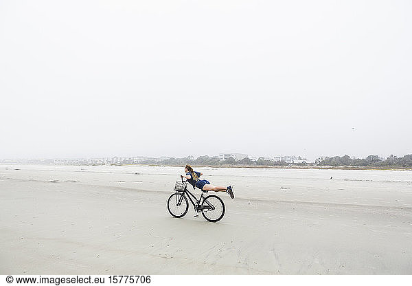 A teenage girl biking on a sandy beach by the ocean