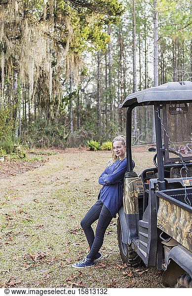 A teenage girl by an all terrain vehicle  a buggy  leaning with arms folded.