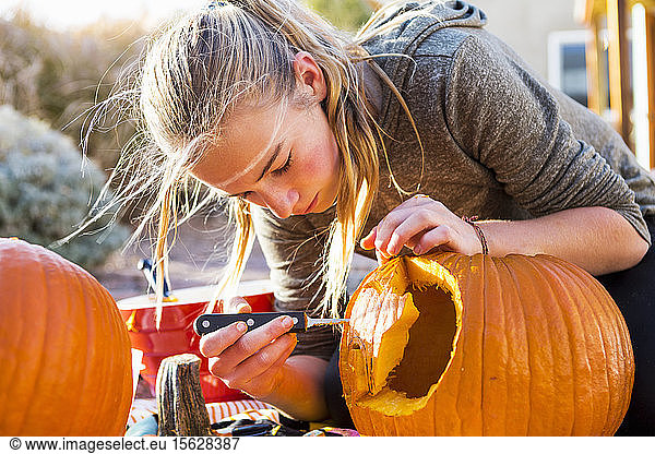 A teenage girl carving a large pumpkin at Halloween.