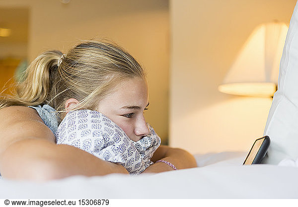 A teenage girl lying on hotel room bed looking at smart phone