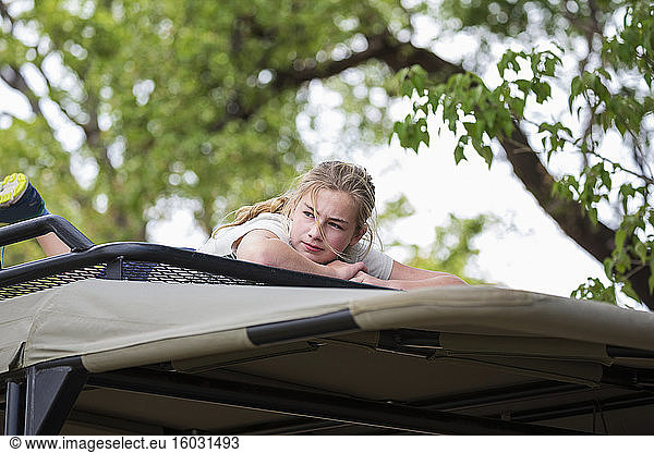 A teenage girl lying on the canopy of a safari vehicle under a tree.