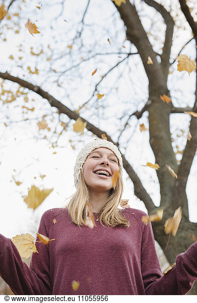 A teenage girl outdoors throwing autumn leaves into the air.