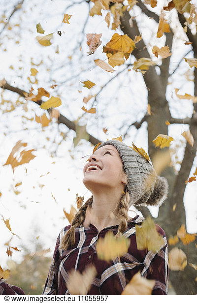 A teenage girl outdoors throwing autumn leaves into the air.