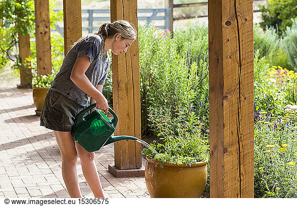 A teenage girl watering plants on porch