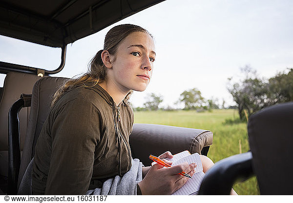 A teenage girl writing in her journal in a safari vehicle in the bush