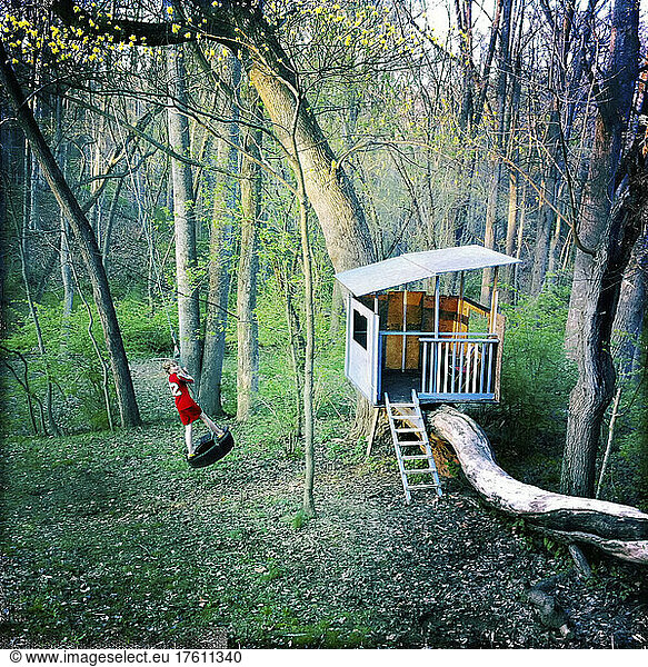 A ten year old boy swings on a tire swing next to a treehouse.; Cabin John  Maryland.
