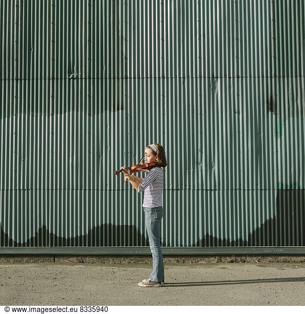 A ten year old girl playing the violin on an urban street.