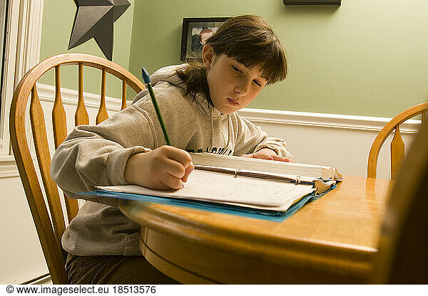 A ten-year-old girl sits at her kitchen table doing her homework on a weekend afternoon.