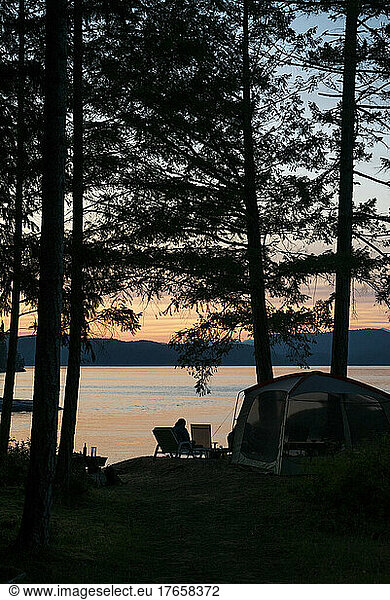 A tent and camp scene among trees overlooking water