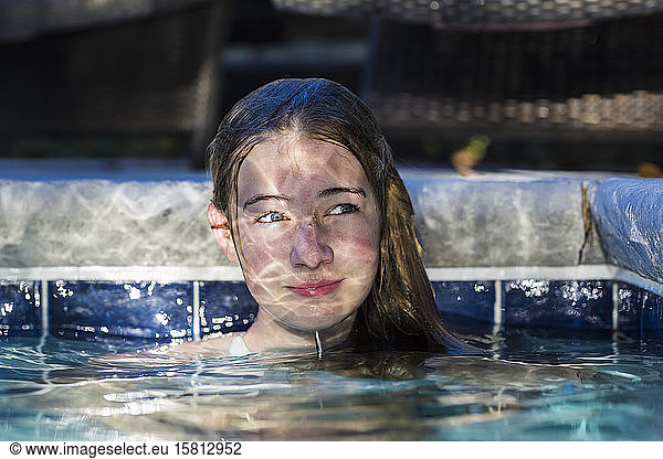 A thirteen year old teenage girl in a swimming pool with reflected light playing on her face