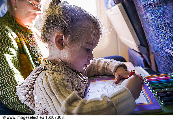 A three year old girl drawing on an airplane