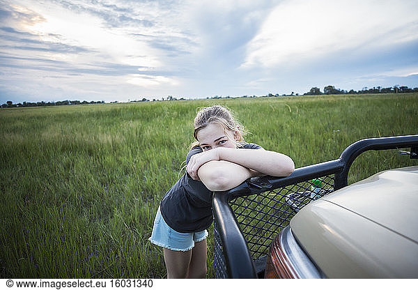 A tired teenage girl leaning on a safari vehicle